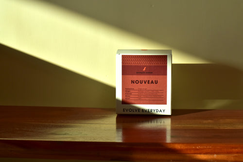 Box labeled 'Nouveau' on a wooden surface with a warm light casting shadows.