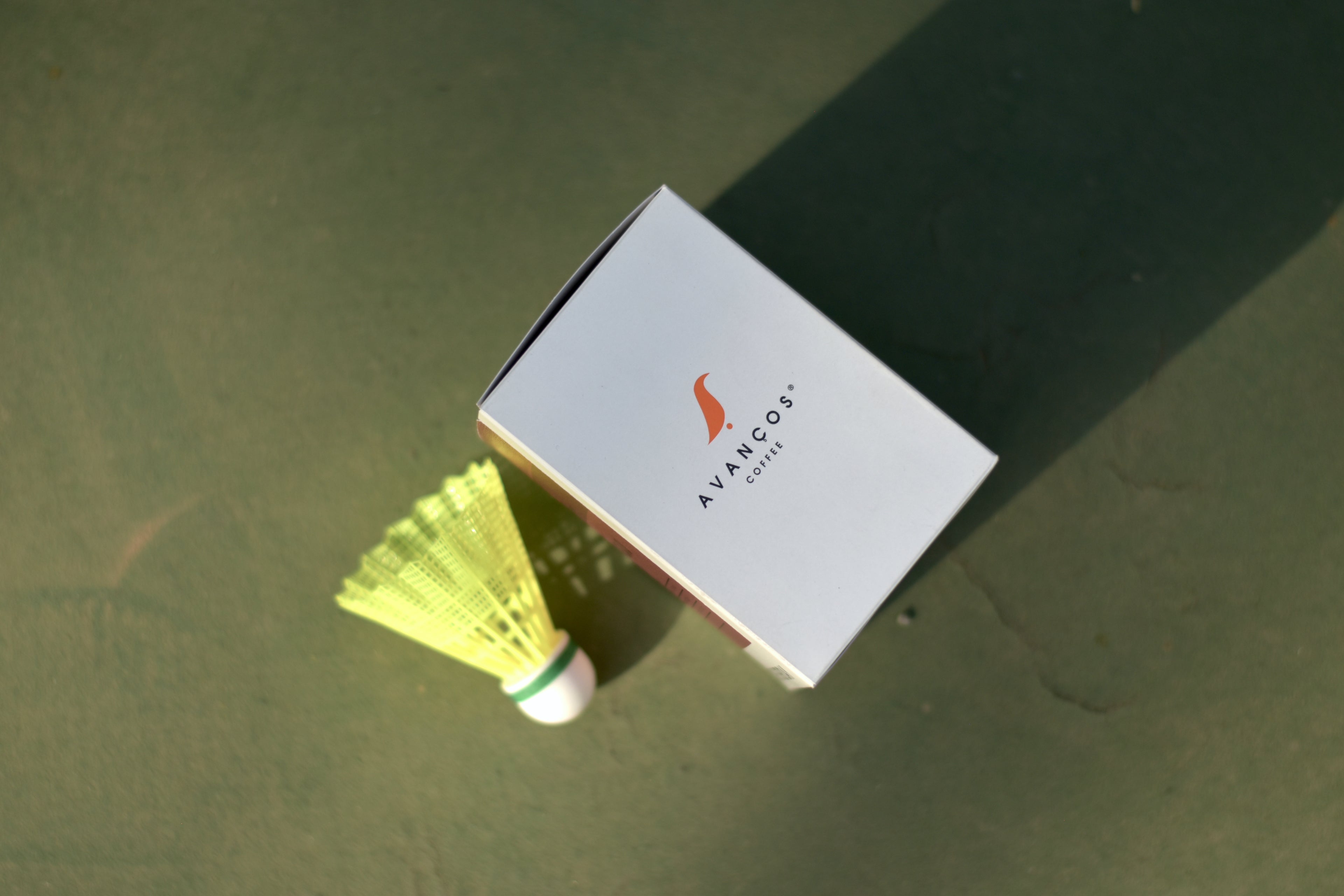 Avancos branded box with a yellow badminton shuttlecock on a green surface